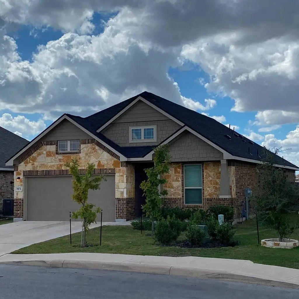 Completed dark architectural shingle roof on a stone and brick San Antonio home under a heavy sky