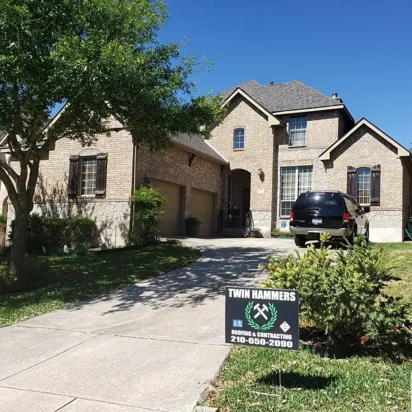 Twin Hammers Roofing yard sign with the company logo and phone number, planted in front of a completed roof replacement