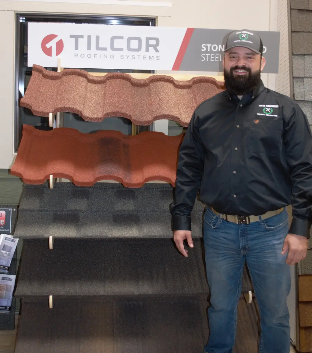 A Twin Hammers team member in a branded cap and shirt beside a Tilcor stone coated steel shingle product display